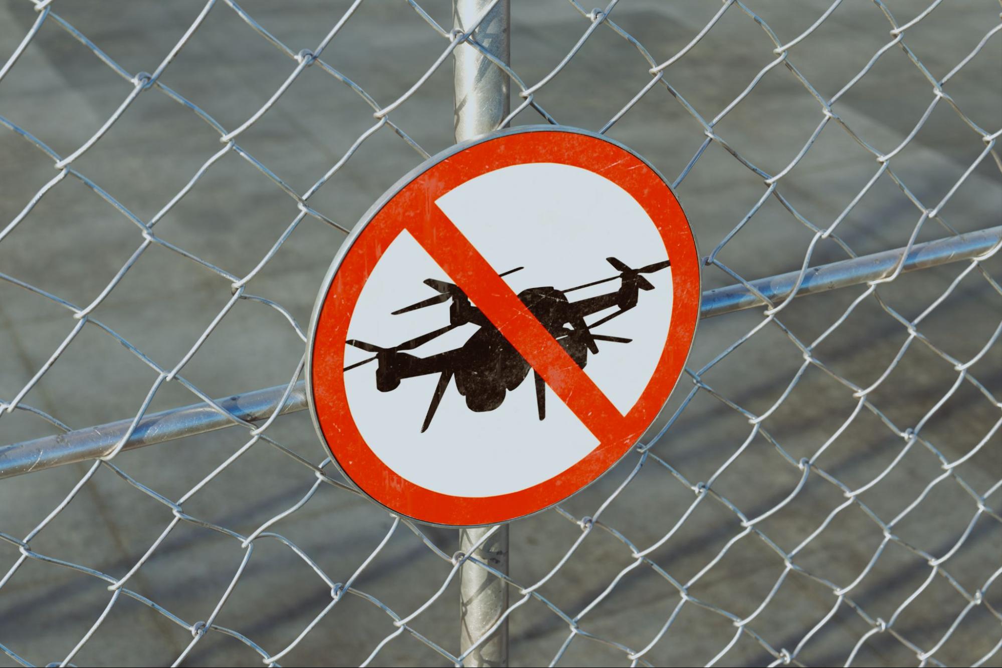 Verbodsbord voor drones op een metalen hekwerk bij een beveiligde locatie.