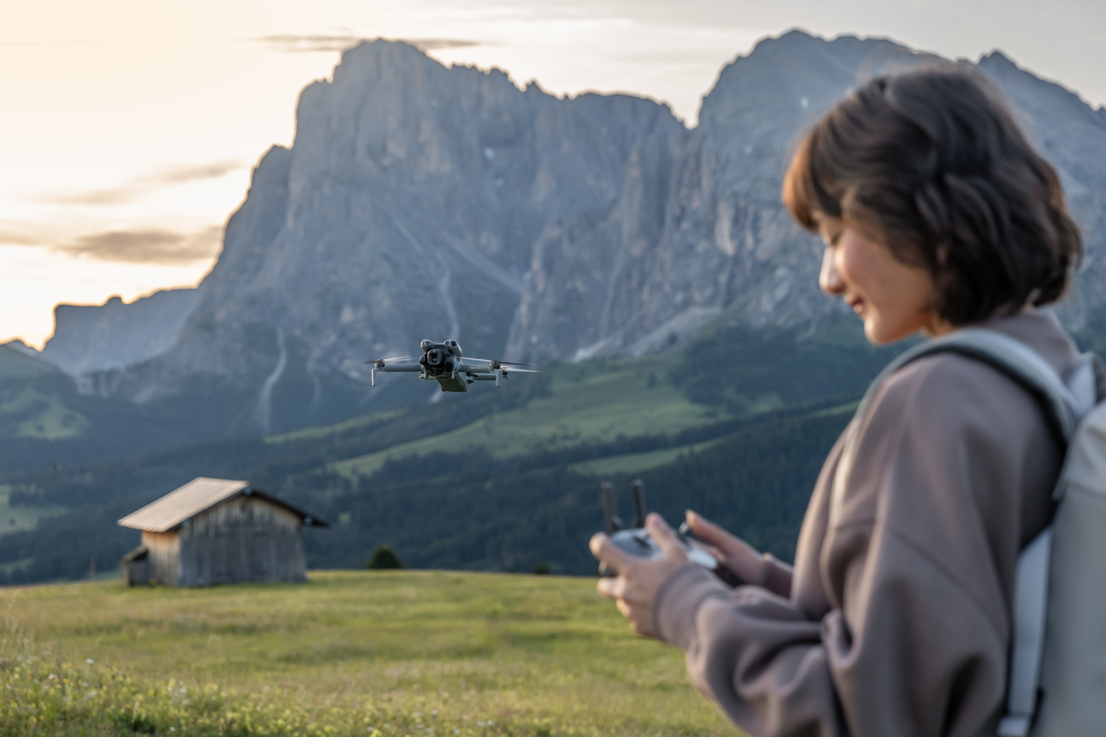 Vrouw laat een drone opstijgen met DJI-controller in een berglandschap bij zonsondergang.