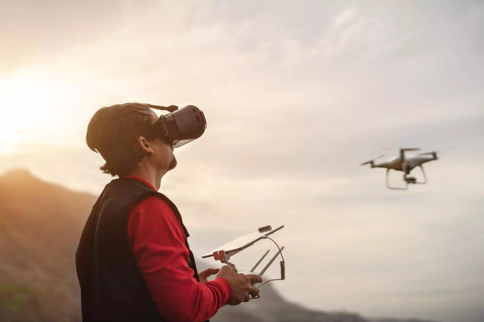 Man met FPV-bril bestuurt een drone in de lucht bij zonsondergang.