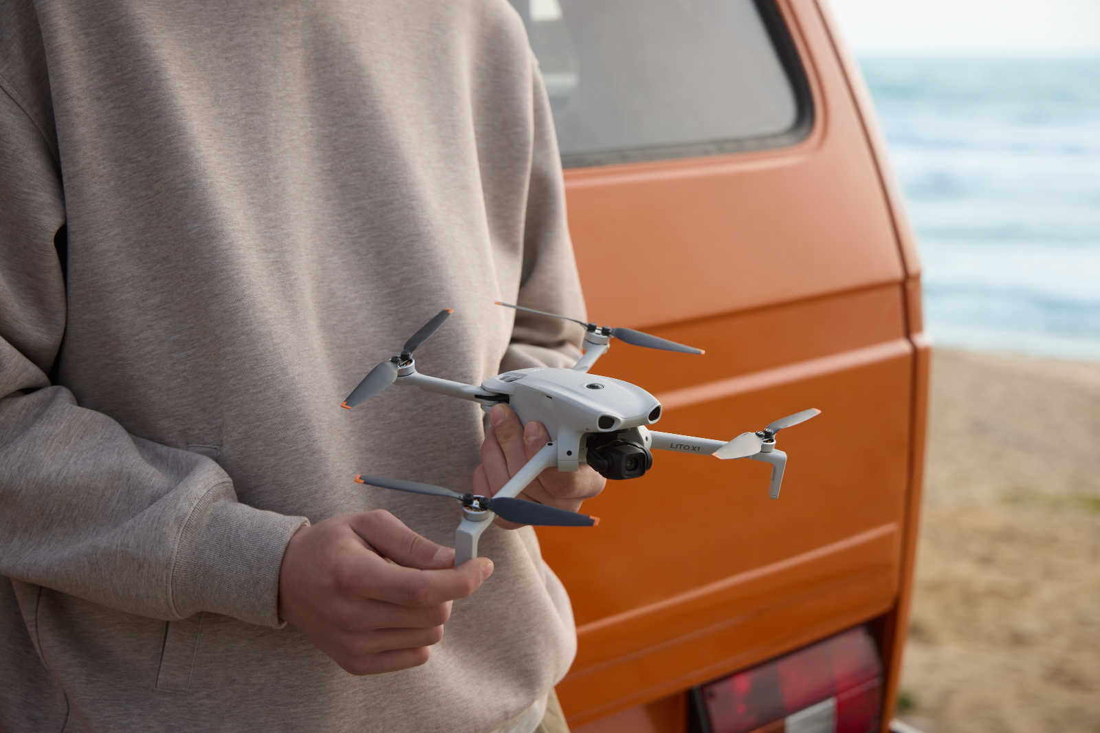 Reiziger houdt een compacte drone vast bij een camper aan zee.